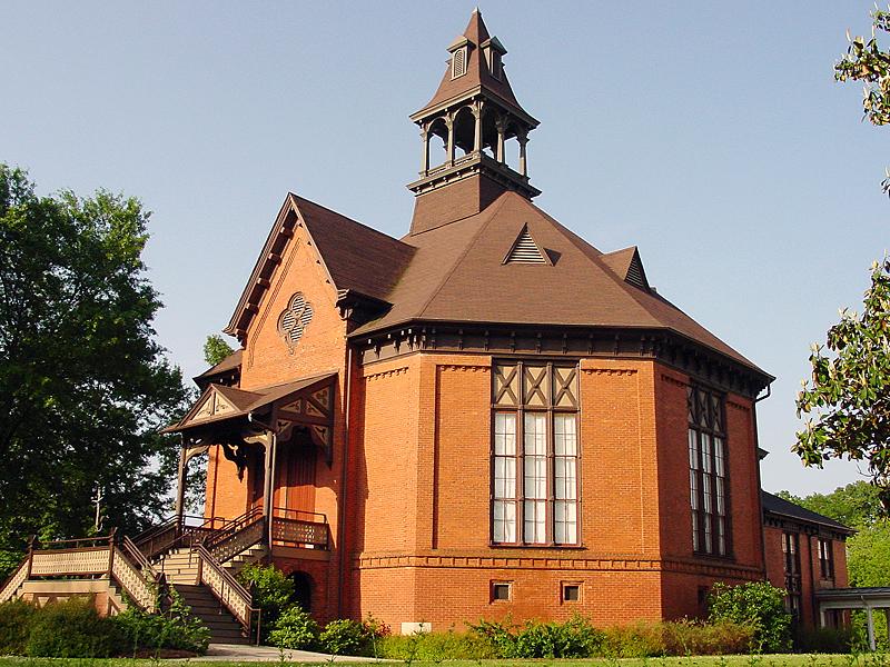 A picture of the octogonal chapel taken from the side. The stairs to the front door are located on the left. The building is made out of orange brick, with Victorian detailing.